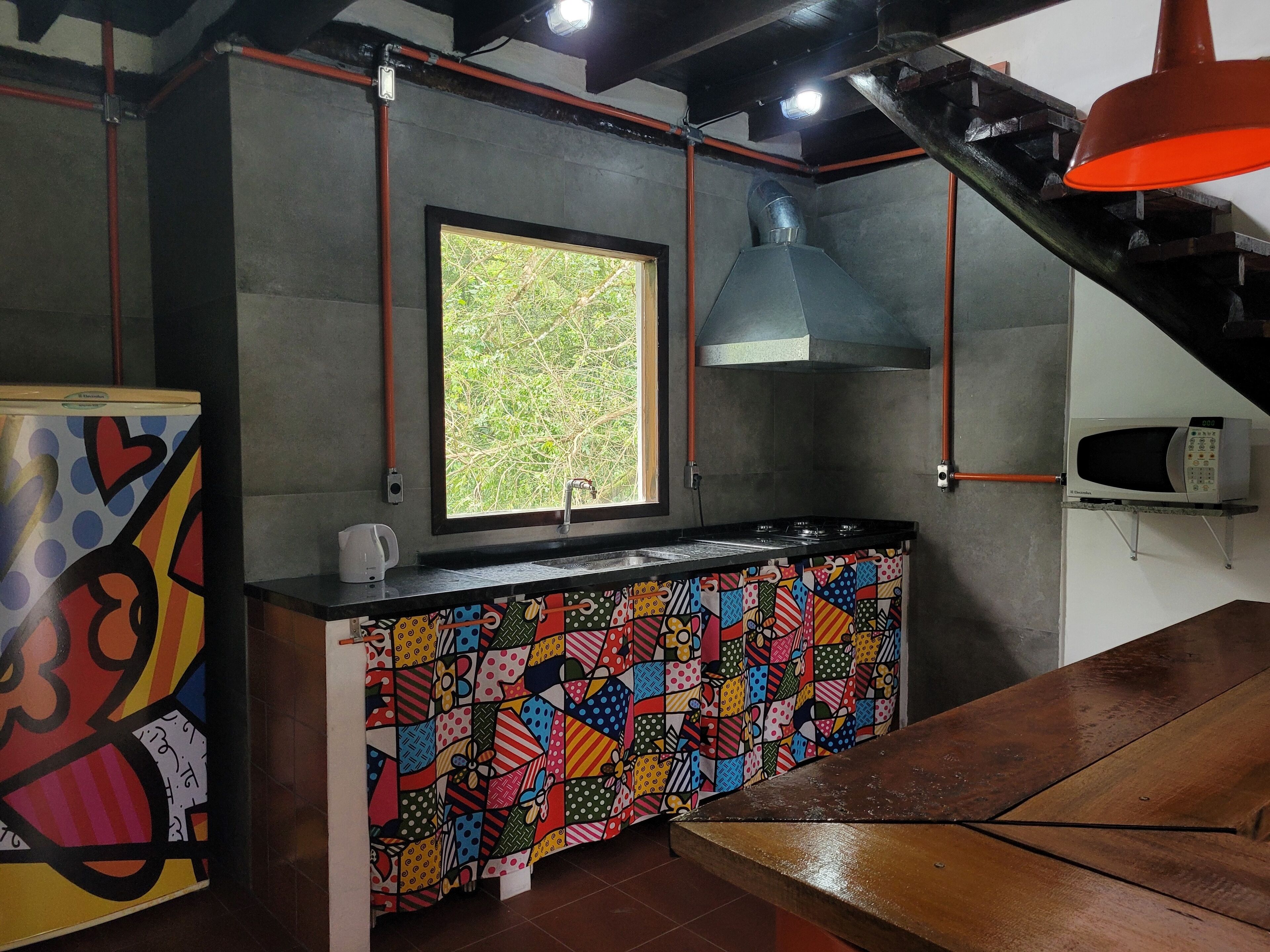 Una cocina con un salpicadero de colores, una ventana con vista a la vegetación y un microondas sobre un pedestal.