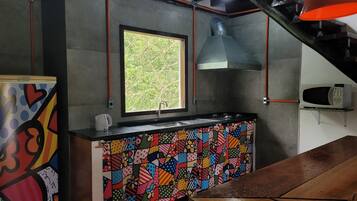 Una cocina con un salpicadero de colores, una ventana con vista a la vegetación y un microondas sobre un pedestal.