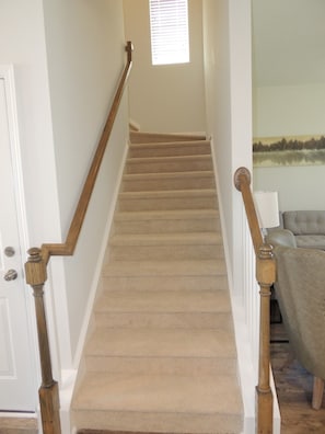 Stairs lead to an upper floor, flanked by white walls and a window with blinds.