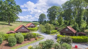A cluster of log cabins with a central driveway, surrounded by lush greenery and trees.