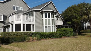Une grande maison à deux étages, à l’extérieur gris et aux ornements blancs, dotée d’une imposante baie vitrée et d’un balcon avec des balustrades blanches.