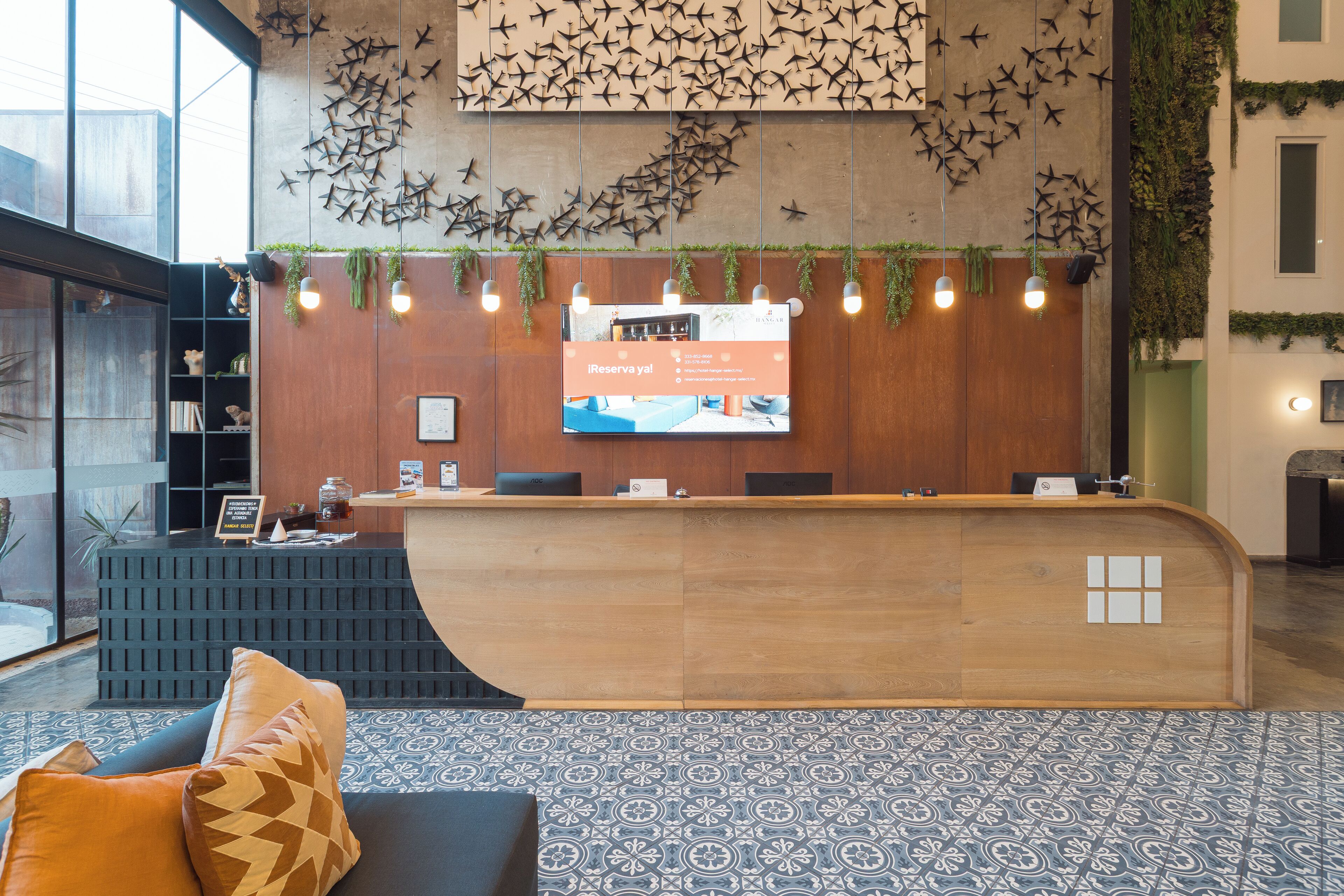 Un espace d’accueil doté d’un comptoir de réception en bois, d’un grand écran affichant des informations et d’un sol à motifs.