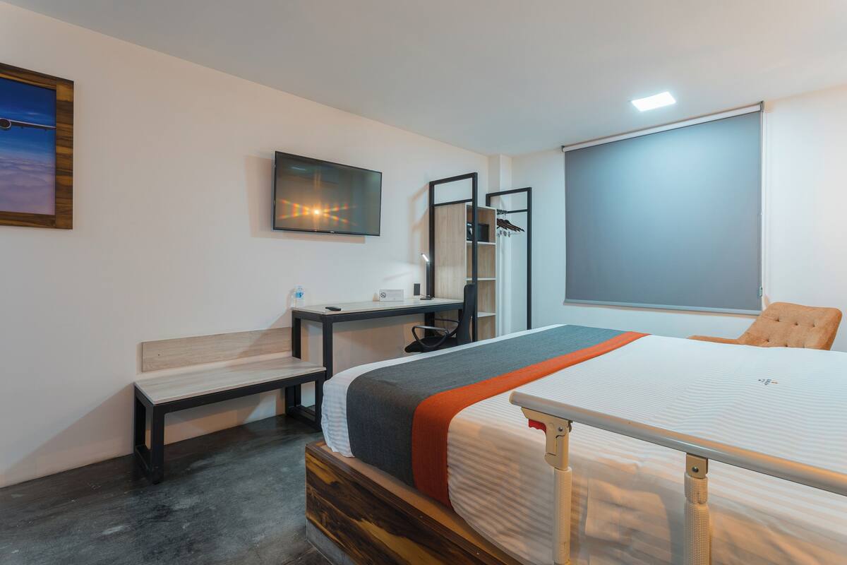 Een moderne slaapkamer met een bed, bureau, stoel en een televisie.