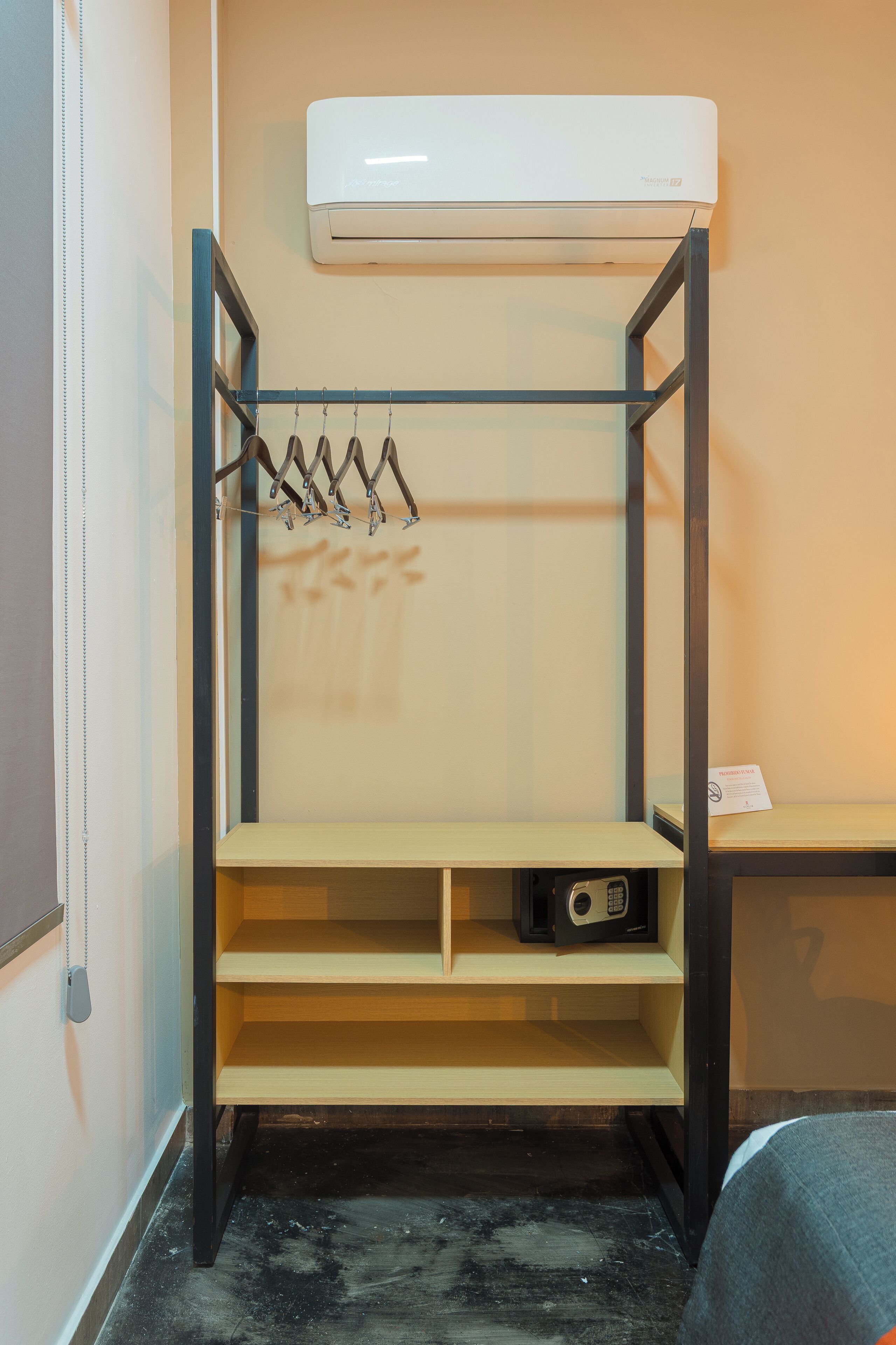 A compact room with a built-in air conditioner, a coat rack, and a small shelf with a radio.