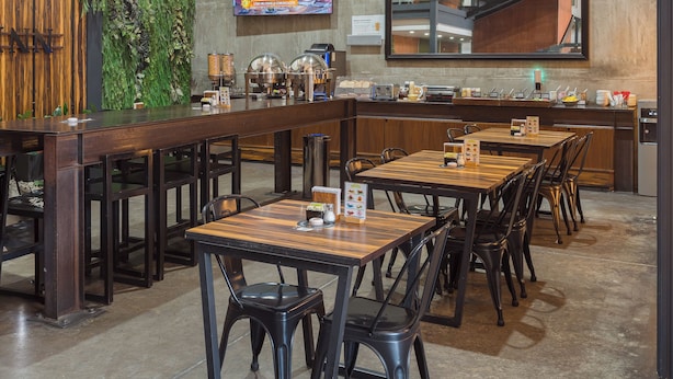 A restaurant with a modern interior, featuring a large TV screen, a wooden bar, and a green wall with plants.