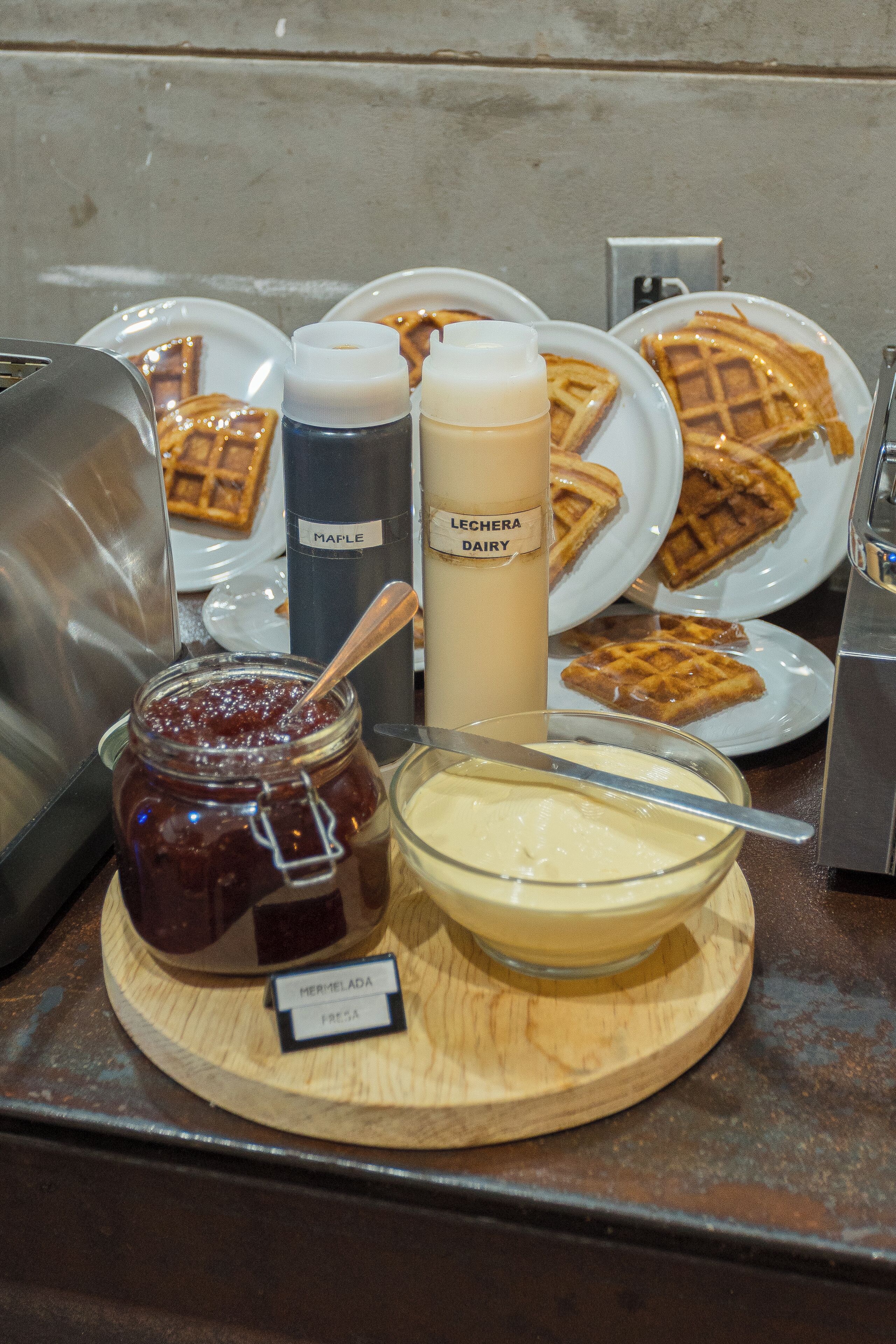 A breakfast buffet with waffles, maple syrup, and a bottle of milk.