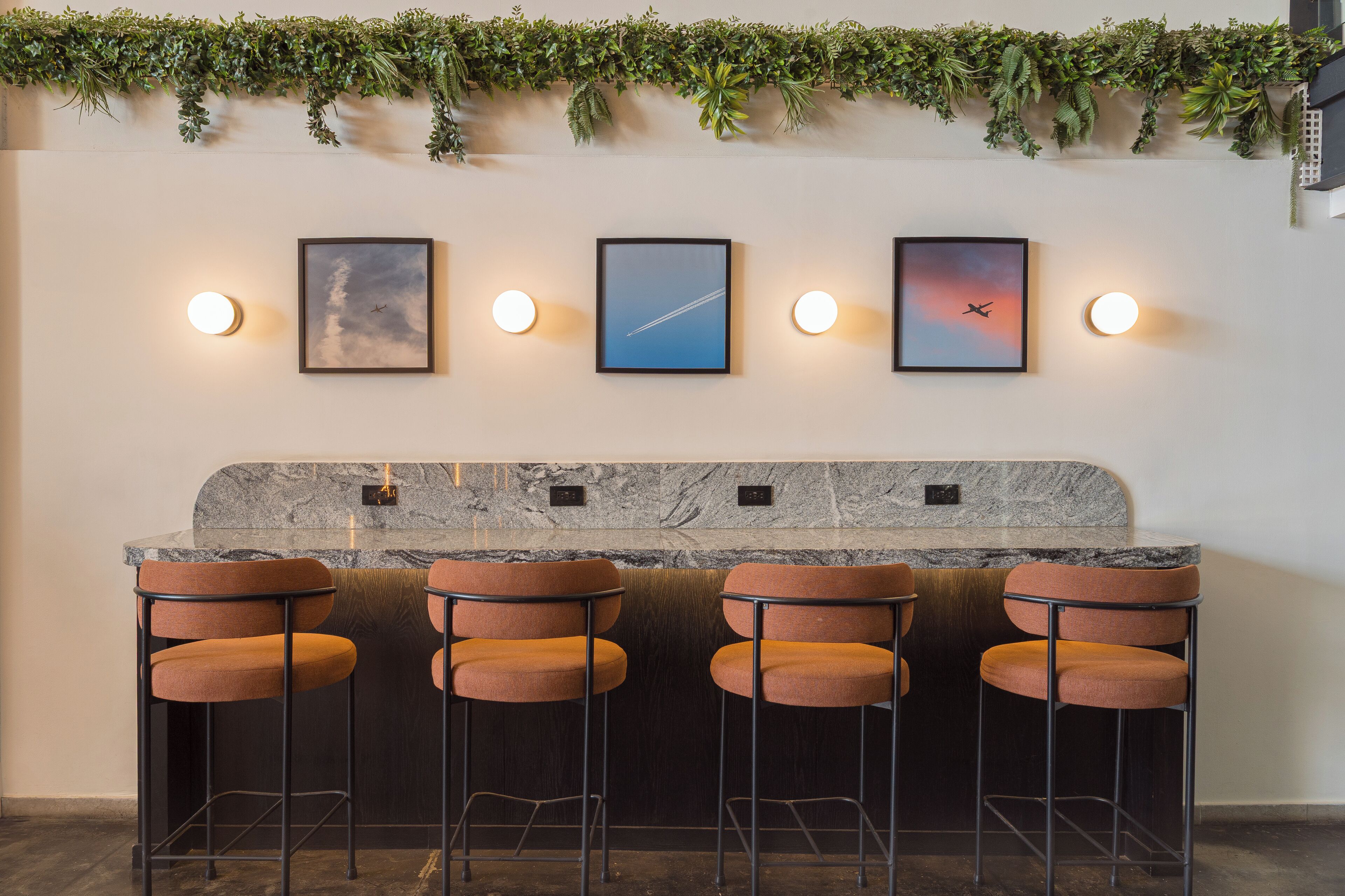A bar area with three stools, a marble countertop, and framed pictures on the wall.