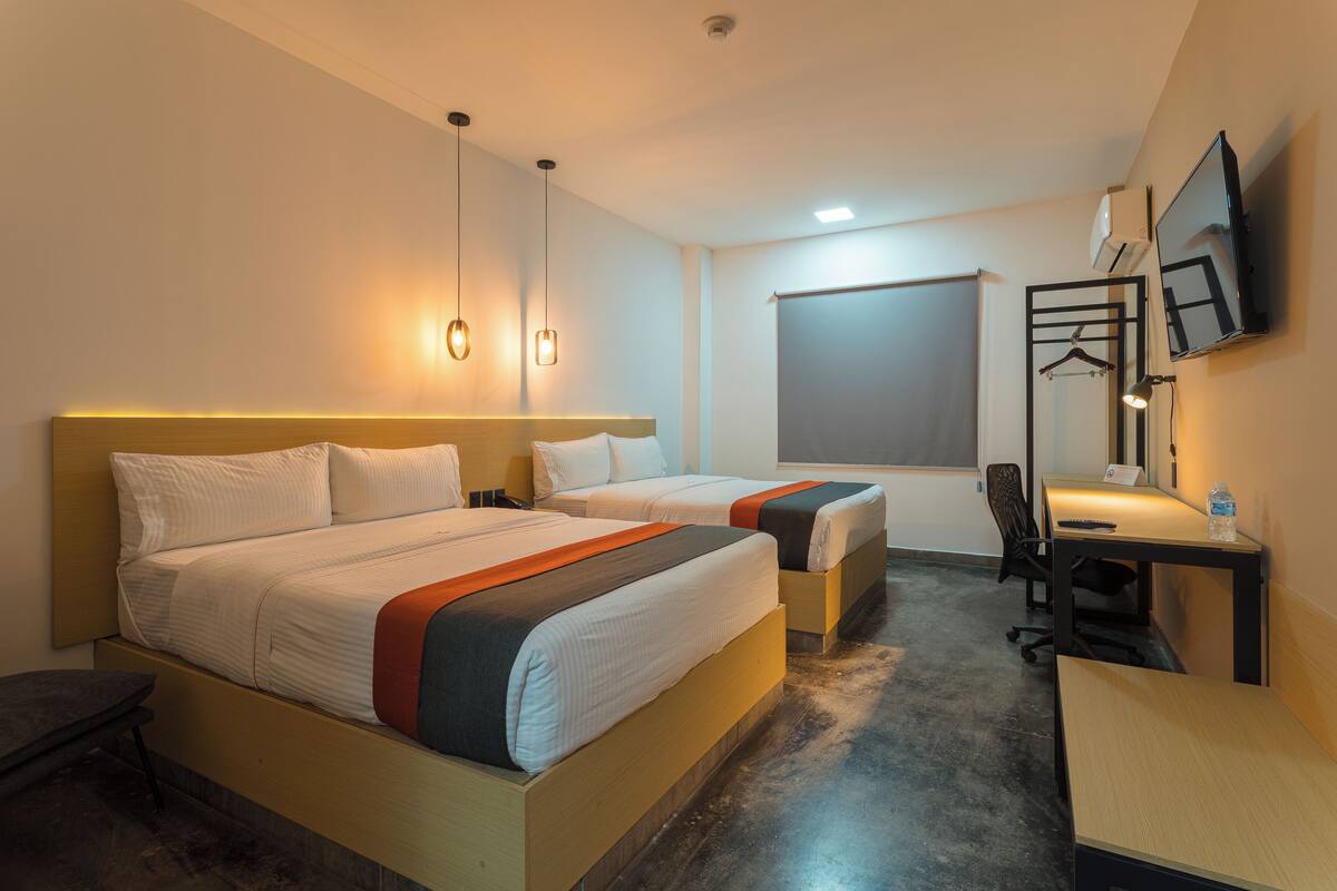 Een hotelkamer met twee bedden, een bureau, een stoel, een televisie en een raam met jaloezieën.