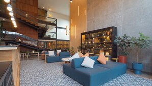 A modern lobby with a blue patterned floor, a staircase, a seating area with sofas, and a large bookshelf.