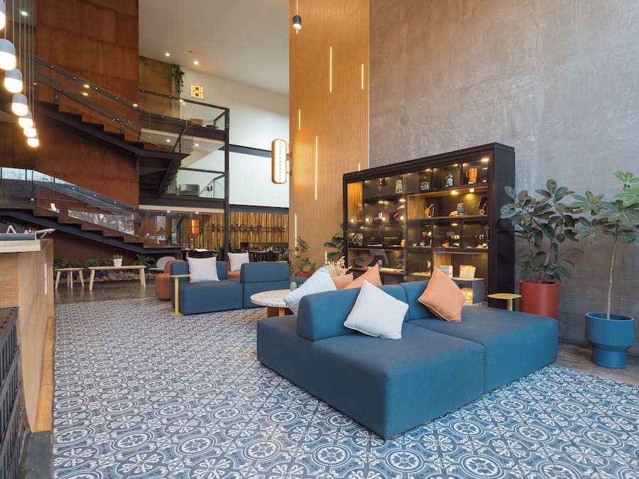 Eine moderne Lobby mit blau gemustertem Boden, einer Treppe, einer Sitzecke mit Sofas und einem großen Bücherregal.