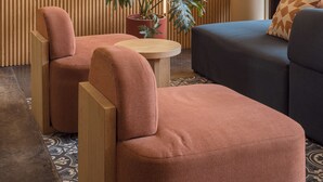 A modern interior with a wooden slat wall, two cushioned chairs, a small round table, and a sofa.