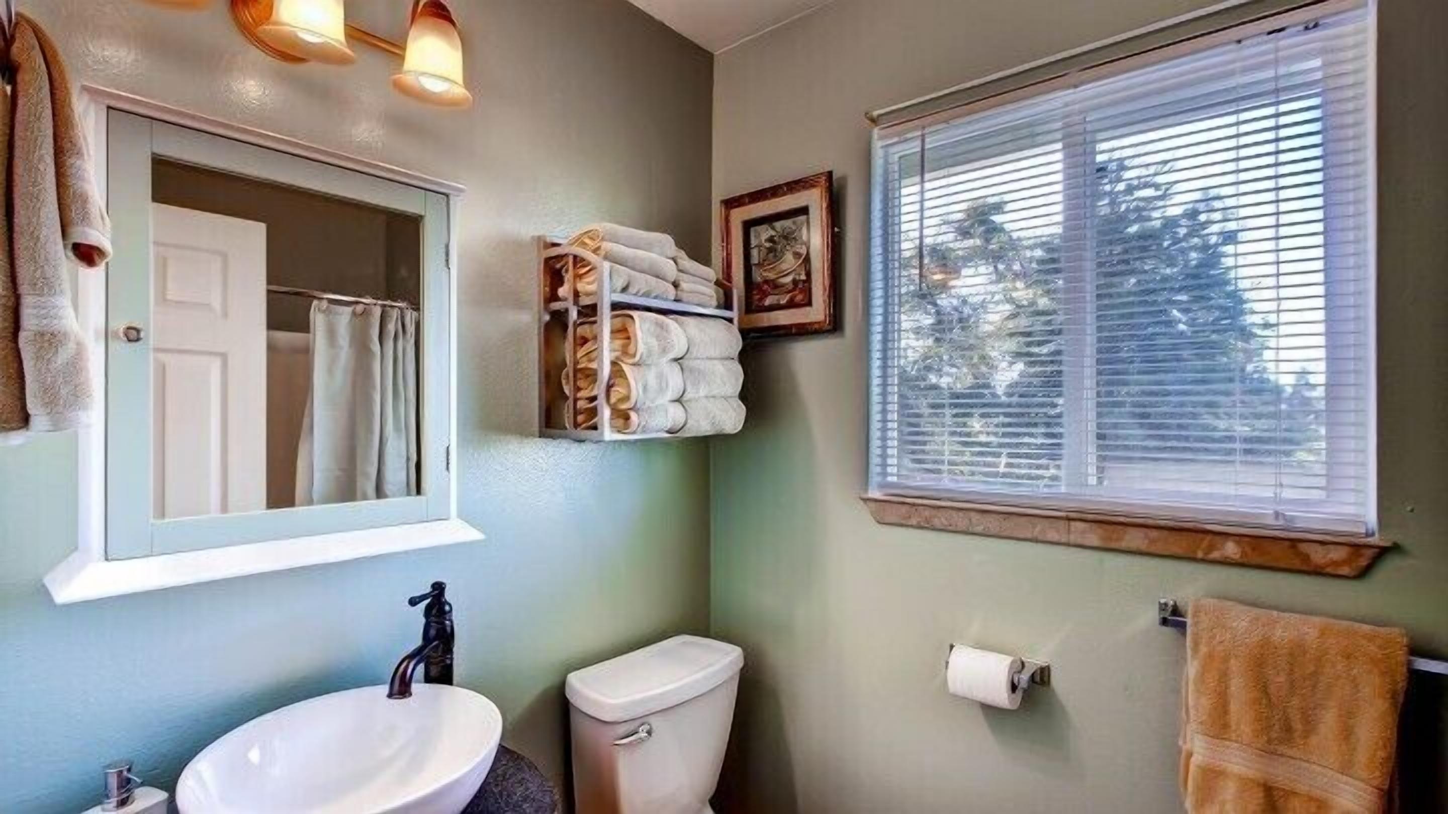 A bathroom with a sink, toilet, towel rack, and a window with blinds.