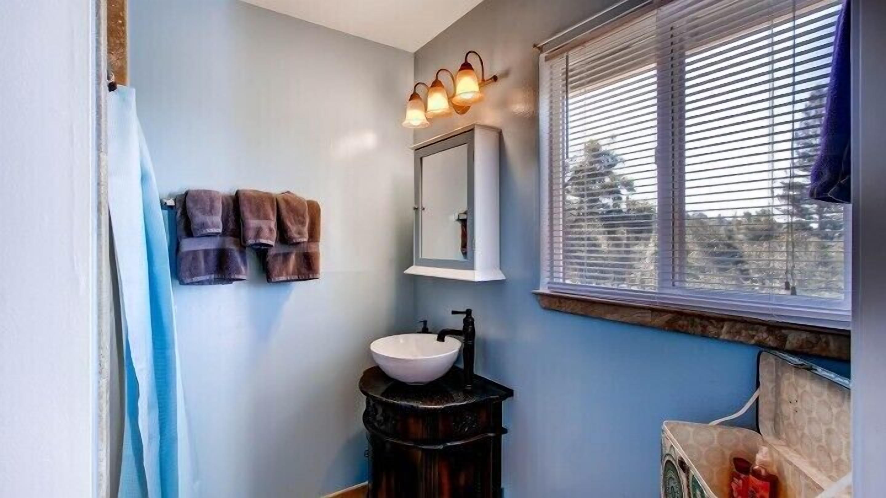 A bathroom with a sink, mirror, towel rack, and window with blinds.
