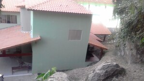 Un edificio con techo de tejas y una ventana pequeña. En primer plano se ve una roca grande y una escalera que sube al edificio.