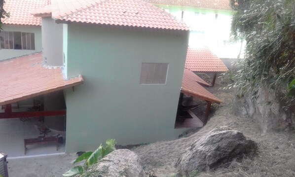 A building with a tiled roof and a small window. There is a large rock in the foreground and a staircase leading up to the building. - OUTHome - Espaço e Sabores (São Sebastião)