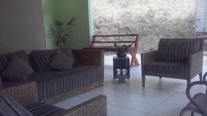 Un espacio de estar al aire libre cubierto con mobiliario de mimbre, una pequeña mesa con dos tazas y un banco.