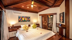 A hotel room with a large bed, wooden ceiling, artwork on the walls, and a small table with a lamp. - Resort Sombra e Água Fresca (Tibau do Sul)