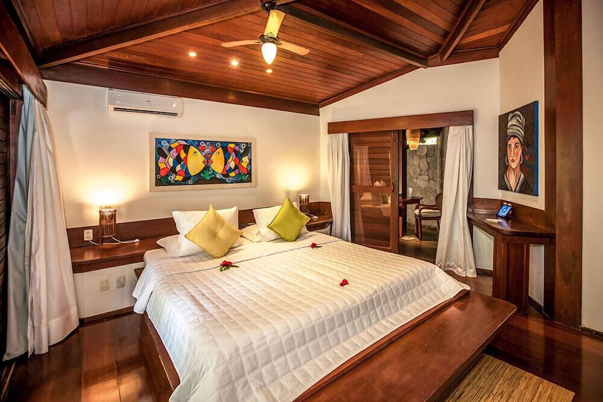 Een hotelkamer met een groot bed, houten plafond, kunstwerken aan de muur en een tafeltje met een lamp.