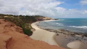 A coastal landscape with a sandy beach, rocky outcrops, and a cliff with vegetation. - Resort Sombra e Água Fresca (Tibau do Sul)