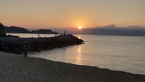 A beach at sunset with a rocky shoreline and a few people walking. - Hotel Gran Juquila Huatulco (Santa María Huatulco)