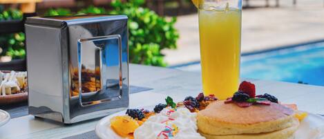 A breakfast setting with pancakes, whipped cream, berries, and a glass of orange juice.