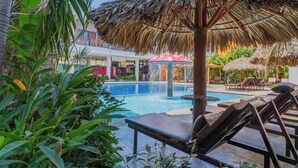 Un área de piscina con sillones de descanso, una sombrilla de paja y una fuente de agua.