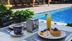 Una mesa de desayuno con una taza de café, un vaso de jugo, una caja, y panqueques con bayas y crema batida.
