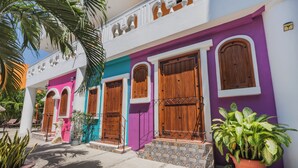 Un edificio colorido con varias puertas y ventanas, rodeado de macetas con plantas y palmeras.