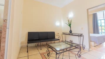 A room with a black sofa, a glass-top table with metal legs, and a potted plant.