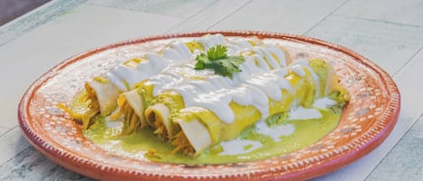 A plate of enchiladas with green sauce and white sauce, garnished with a leaf, on a wooden table.