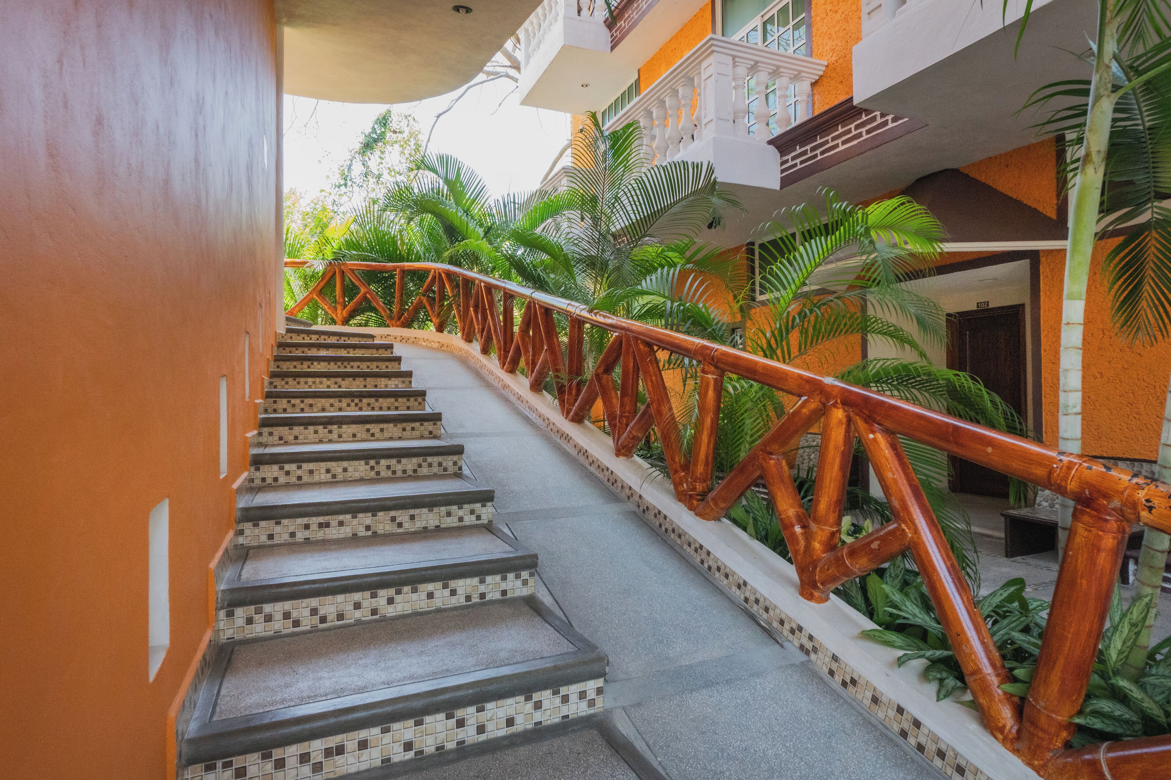 A staircase with a tiled pattern and a wooden railing, surrounded by lush green plants.