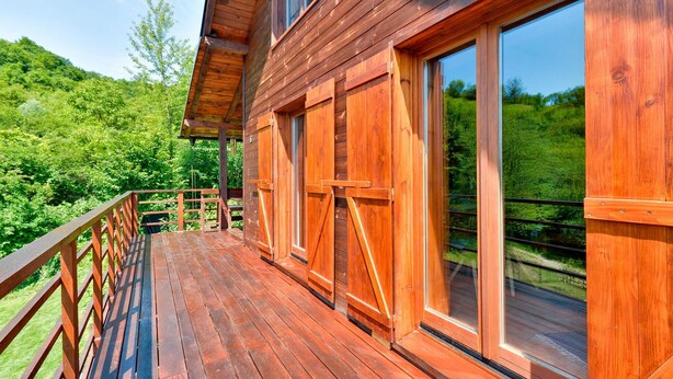 Une cabane en bois dotée d’un balcon, de grandes fenêtres et offrant une vue sur une colline boisée.
