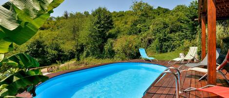 A swimming pool with a wooden deck, surrounded by lush greenery and trees.