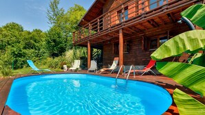 Une cabane en bois avec une piscine, entourée de chaises longues et de plantes tropicales.