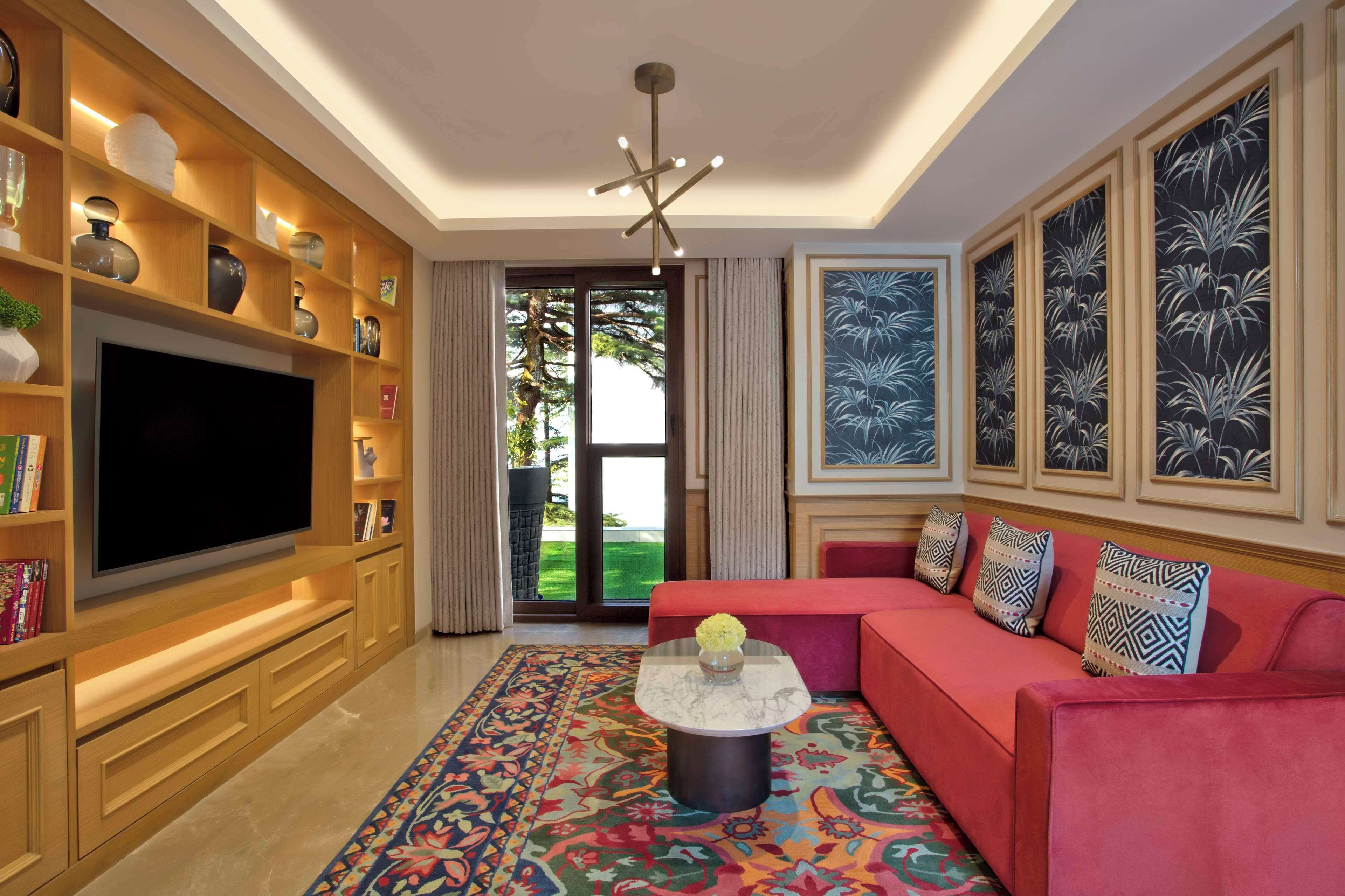 Una sala de estar moderna con un televisor de pantalla plana grande, un sofá rojo, alfombras estampadas y objetos decorativos en estanterías.