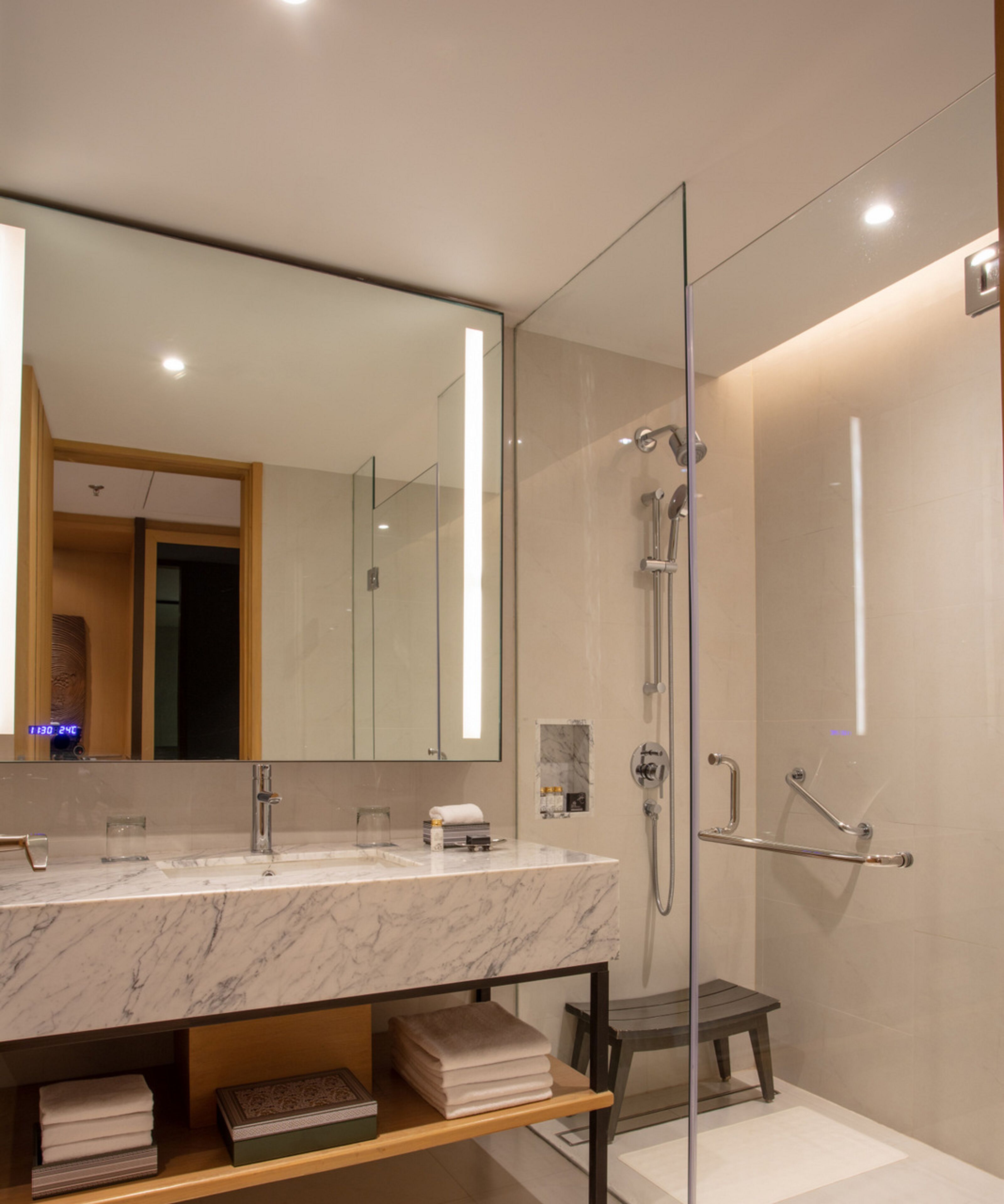 A modern bathroom with a marble sink, a glass shower enclosure, and a large mirror.