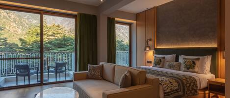 A hotel room with a large bed, a sofa, a small table, and a balcony with chairs.