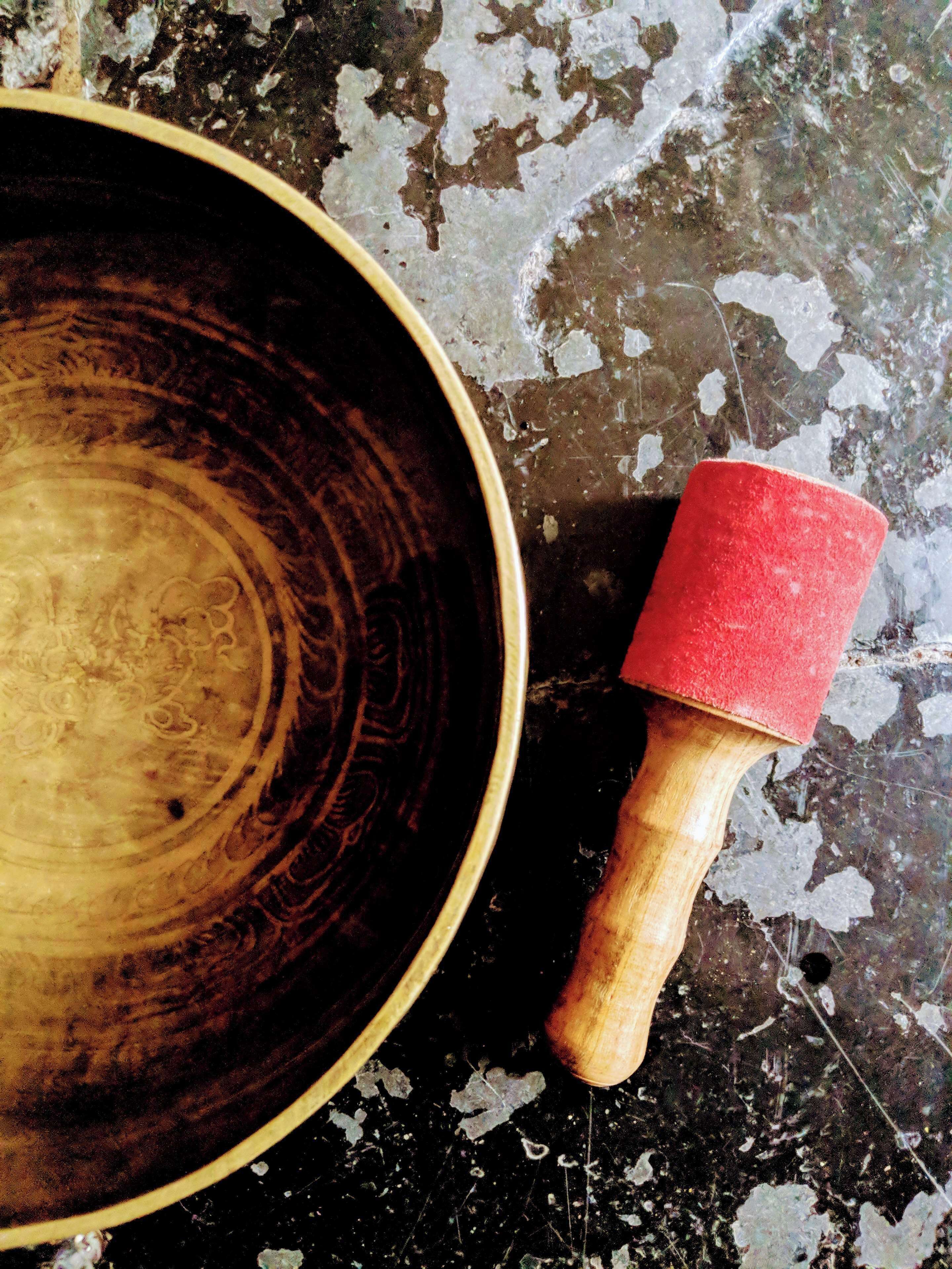 A wooden bowl with a red handle on a textured surface.