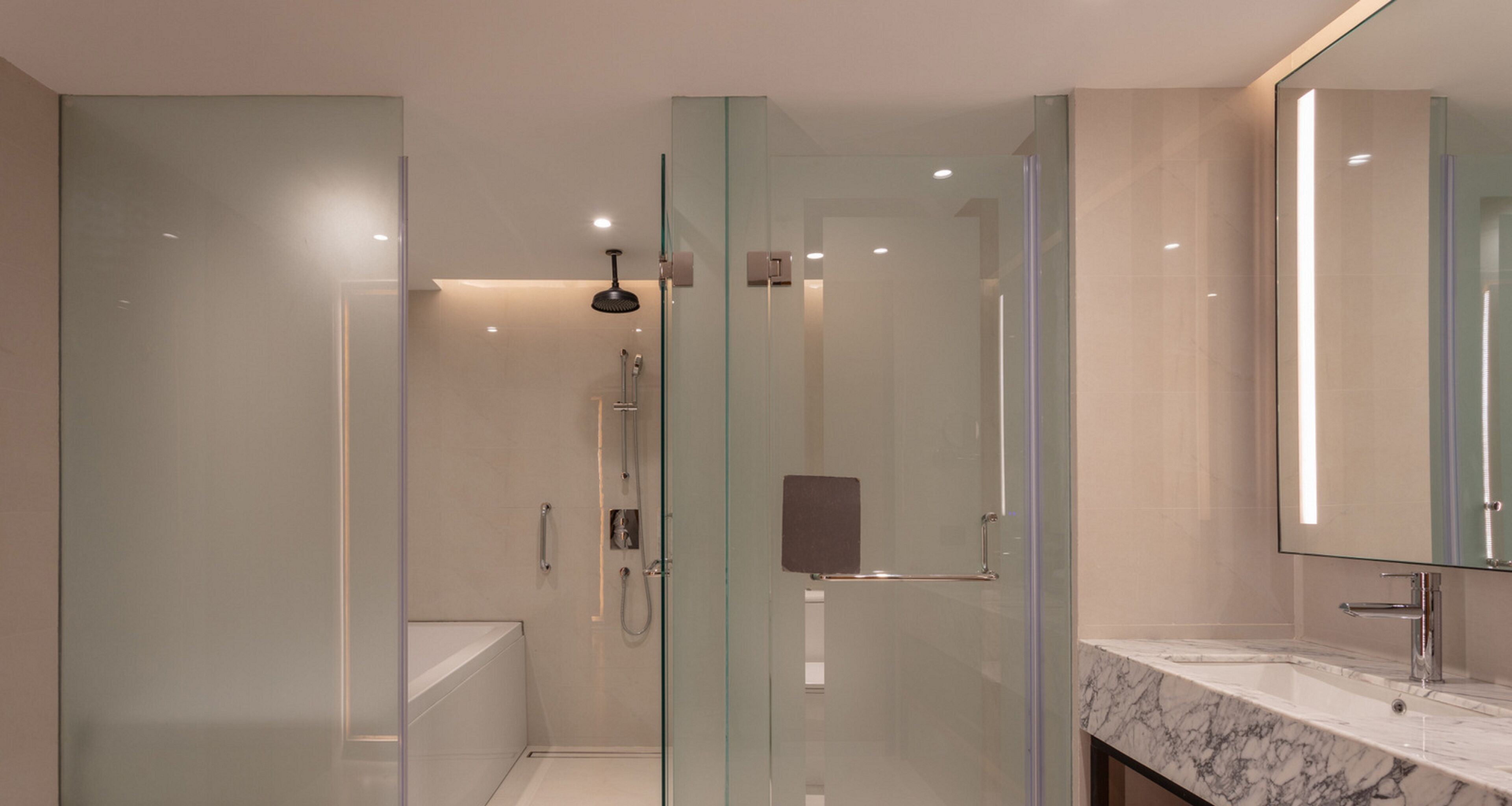 Ein modernes Badezimmer mit einer gläsernen Dusche, einer weißen Badewanne und einer Marmorwaschtischplatte mit Waschbecken.