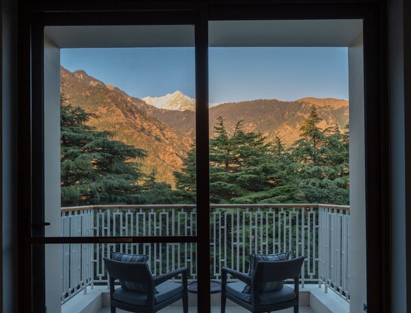 A balcony with two wicker chairs and a white metal railing, overlooking a mountainous landscape with trees and a clear sky. - Hyatt Regency Dharamshala Resort (Dharamshala)