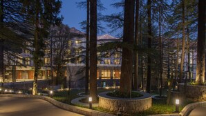 A resort with a large building surrounded by tall trees, a landscaped garden, and a paved walkway. - Hyatt Regency Dharamshala Resort (Dharamshala)