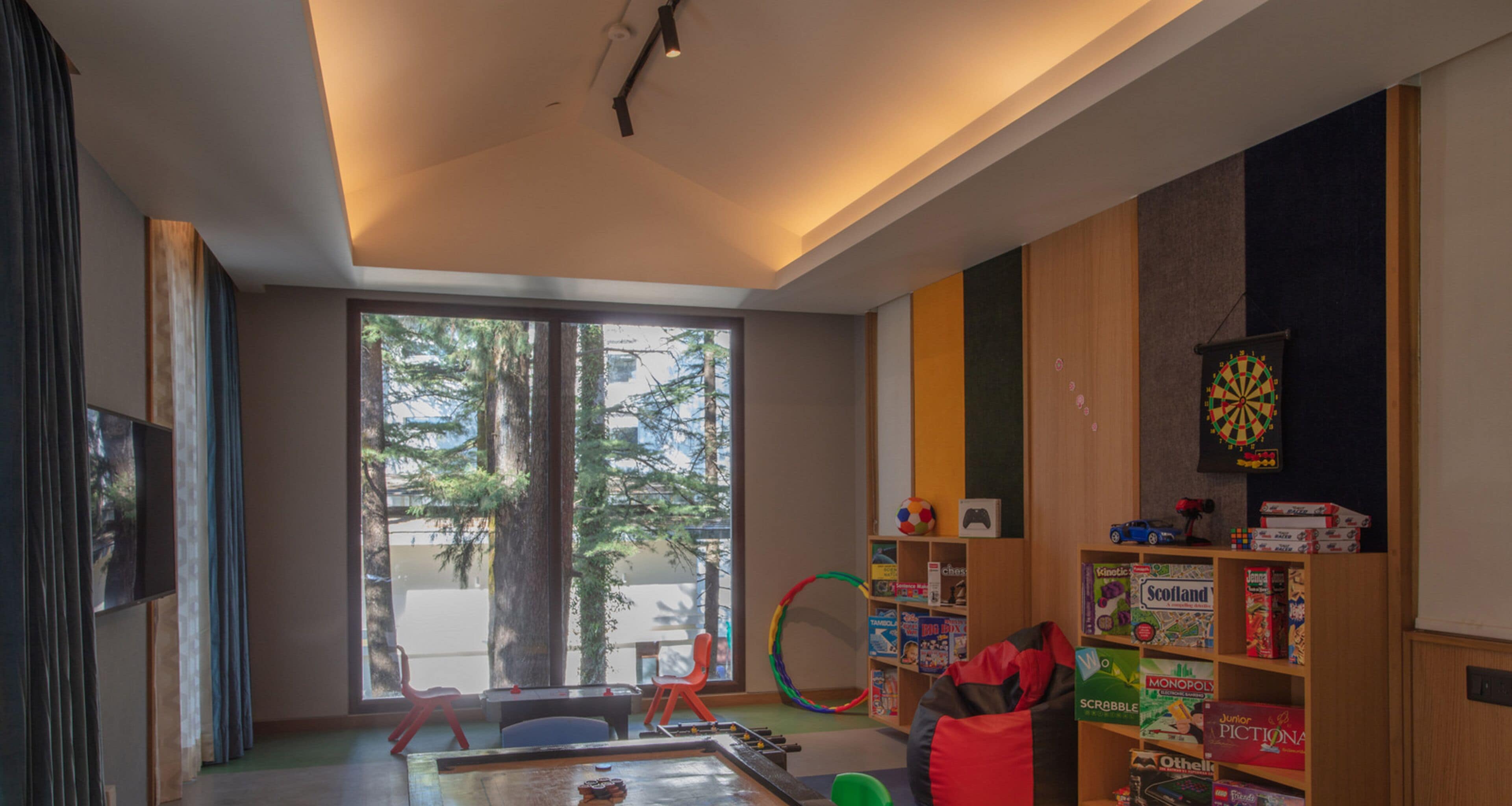 Uma sala de estar moderna, com uma janela grande, um alvo de dardos e uma estante repleta de jogos de tabuleiro.