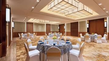 Un amplio salón de banquetes con mesas redondas, sillas blancas y un techo alto con iluminación empotrada.
