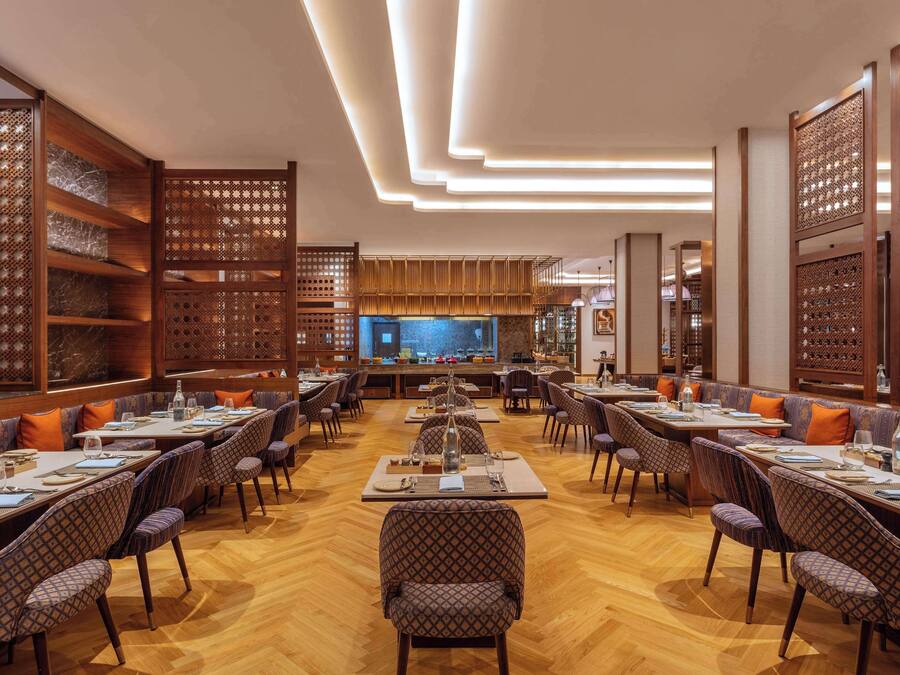 Een ruim restaurant met hoge plafonds, houten lambrisering en een bar in het midden.
