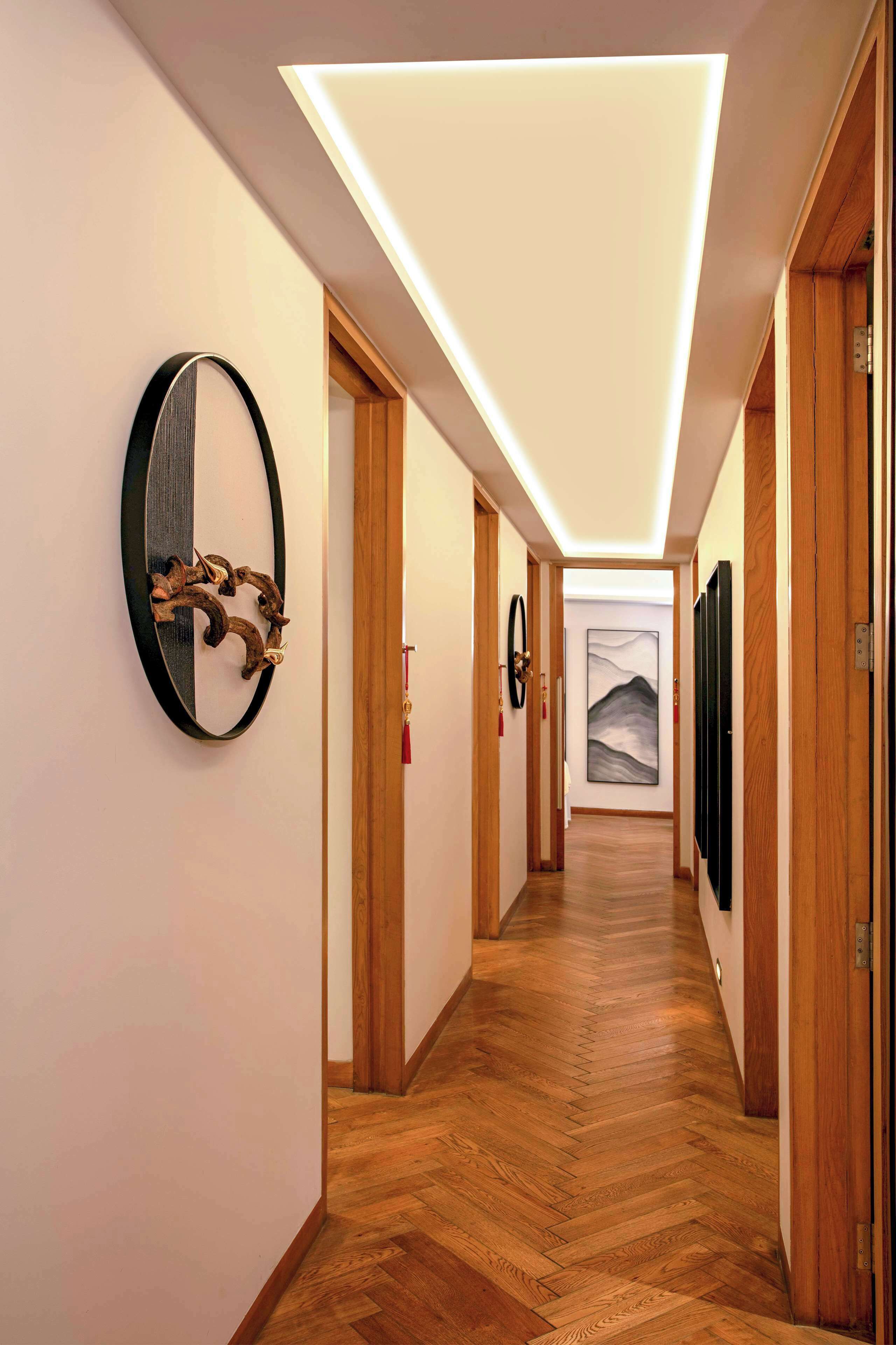 Un couloir doté d’un plancher en bois, d’un luminaire au plafond et d’une œuvre d’art encadrée accrochée au mur.