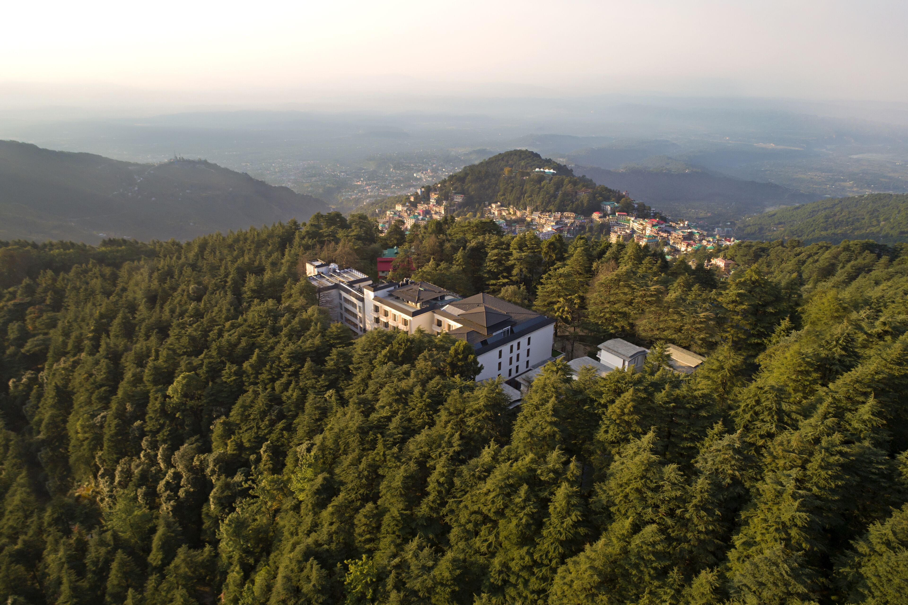 An aerial view of a mountainous area with a cluster of buildings surrounded by dense forest.