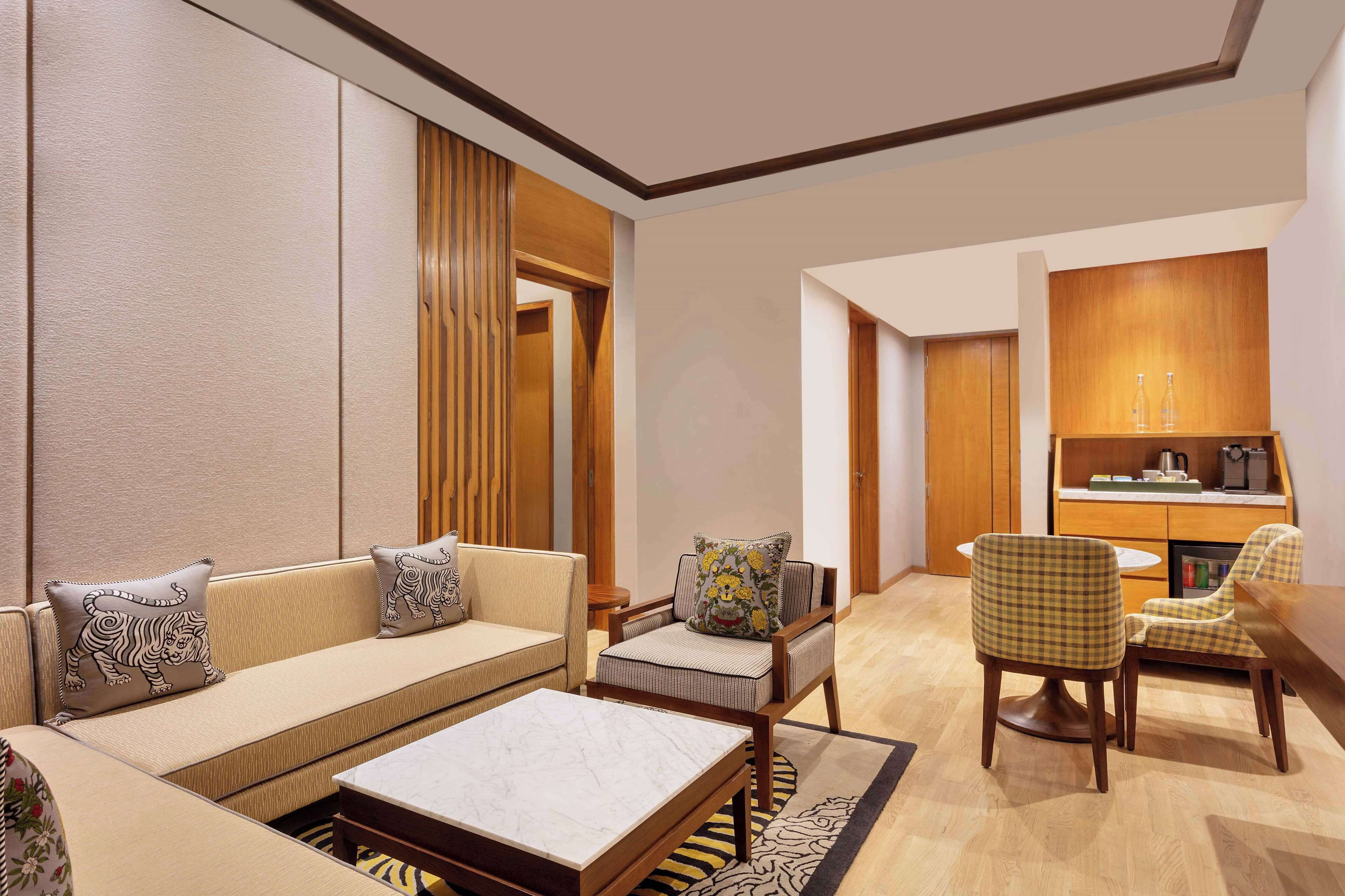 A modern living room with a sofa, armchairs, a coffee table, and a kitchen area with wooden cabinets and a dining table.