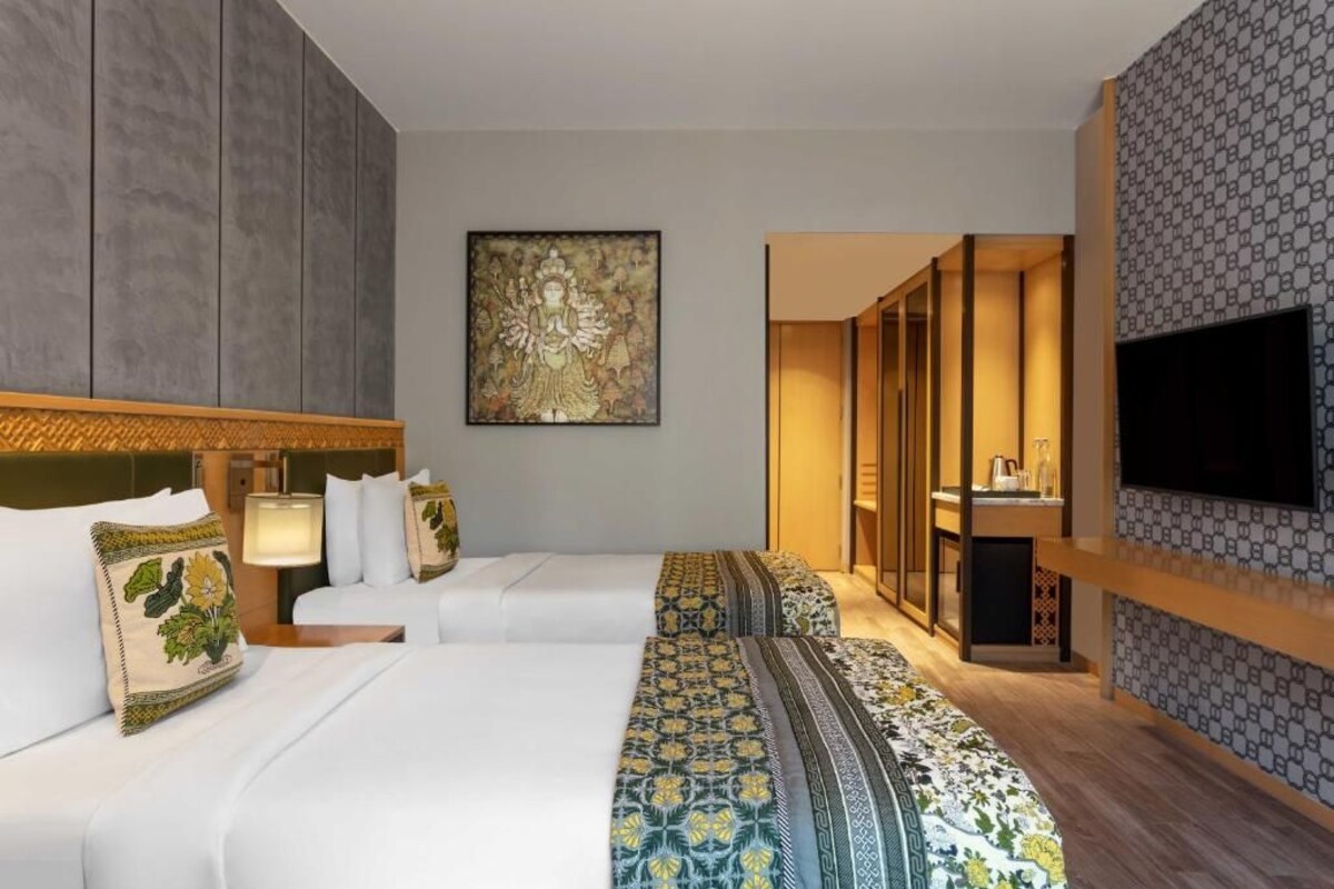 A hotel room with two beds, a television, a bathroom, and a hallway.