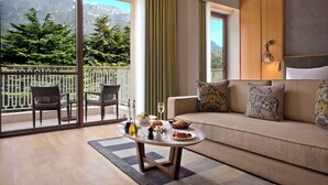 A modern living room with a sofa, a dining table, and a view of a balcony with outdoor furniture. - Hyatt Regency Dharamshala Resort (Dharamshala)