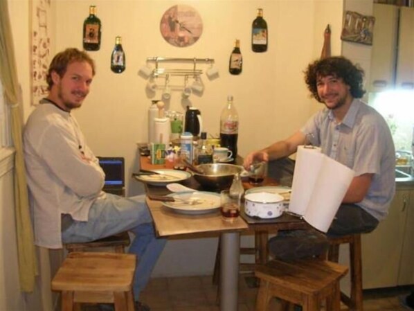 Una cocina con dos taburetes, una mesa con diversos objetos y botellas en la pared.